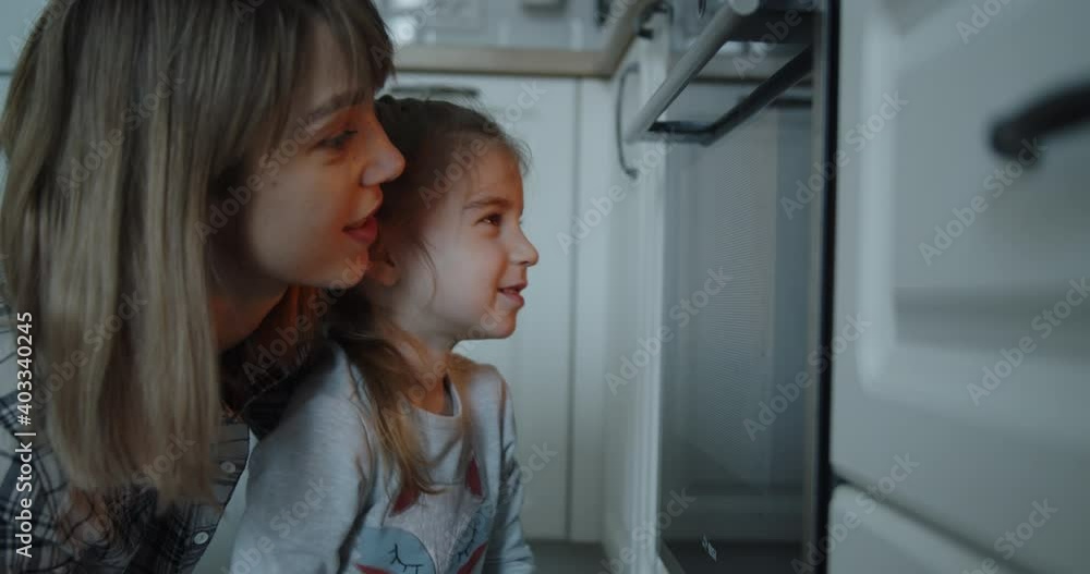 Mother and daughter having fun baking cooking christmas cookies pastry in the kitchen. Loving happy mom and daughter watch as cookies are prepared in the oven. Mother and daughter having fun baking cooking christmas cookies pastry in the kitchen. Loving happy mom and daughter watch as cookies are prepared in the oven.