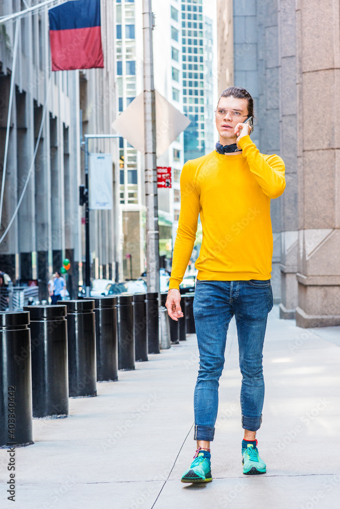Φωτογραφία Young Hispanic American with hair backward, wearing glasses, yellow long sleeve T shirt, blue jeans, green sneakers, black scarf around neck, walking on street in New York City, talking on cell phone