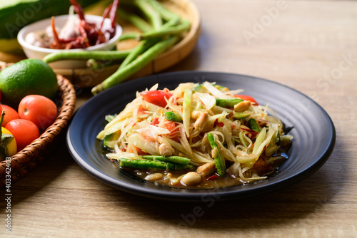 Thai food (Som tum), Spicy green papaya salad with vegetables on wooden table