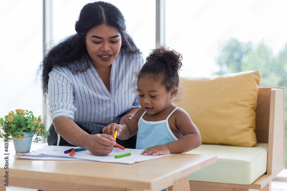Happy African American mother and her little daughter. Mother teaching her daughter drawing and painting. Mom spending time with her daughter. Happy family at home Happy African American mother and her little daughter. Mother teaching her daughter drawing and painting. Mom spending time with her daughter. Happy family at home