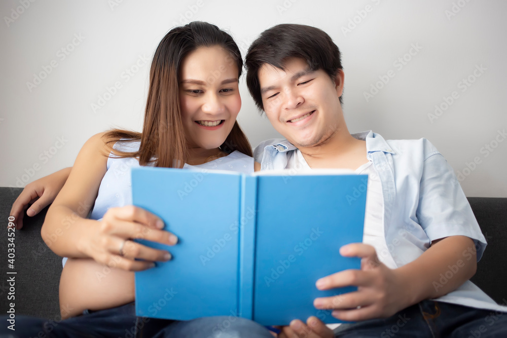 Pregnant Asian woman with her husband reading on the sofa in the house. Pregnant Asian woman with her husband reading on the sofa in the house.