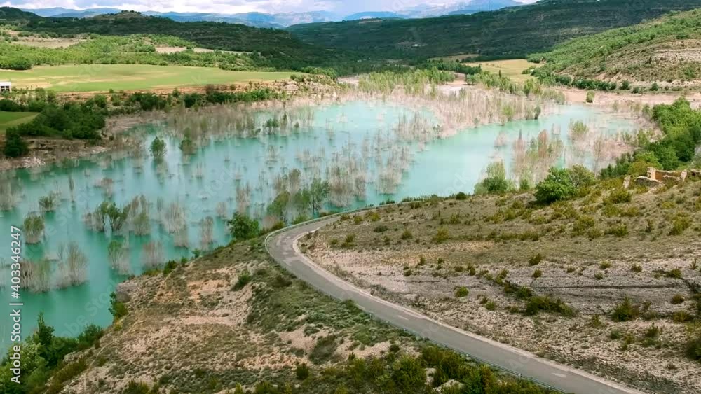 Car moving along the curved road next to Spain mountain cover covered with water, drone covering water flow along Spain ridges. Car moving along the curved road next to Spain mountain cover covered with water, drone covering water flow along Spain ridges.