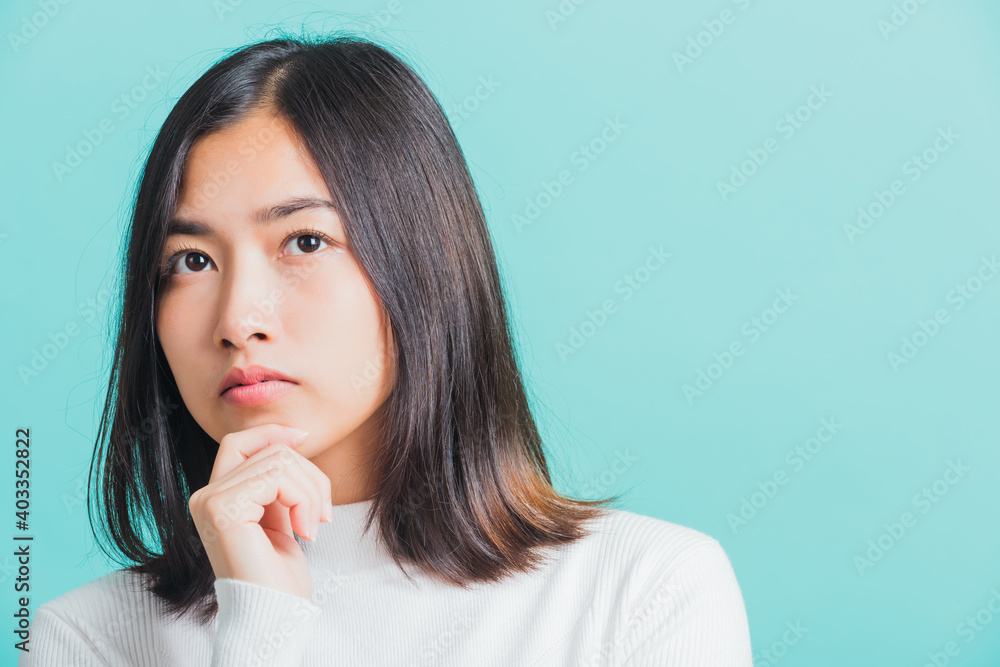 Young beautiful Asian woman hand near the face and thinking, Portrait female touch chin dream dreamy having doubts, studio shot isolated on a blue background Young beautiful Asian woman hand near the face and thinking, Portrait female touch chin dream dreamy having doubts, studio shot isolated on a blue background