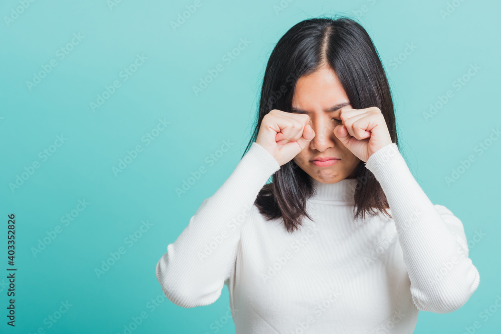 Young beautiful Asian woman displeased upset female frowns face as going to cry, Portrait sad female unhappy wiping tears, studio shot isolated on a blue background Young beautiful Asian woman displeased upset female frowns face as going to cry, Portrait sad female unhappy wiping tears, studio shot isolated on a blue background