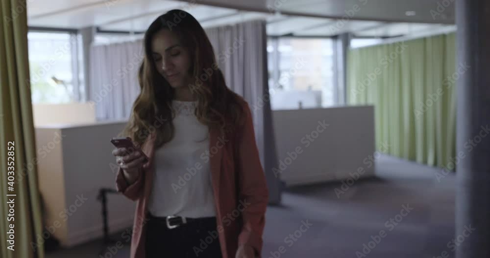 Young woman entrepreneur texting on her phone smiling in a startup business environment standing Young woman entrepreneur texting on her phone smiling in a startup business environment standing