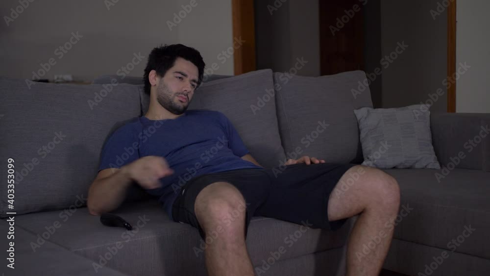 A bored and tired young man is sitting on the sofa in the living room and watching TV. Not finding an interesting TV channel, the person turns off the TV and leaves A bored and tired young man is sitting on the sofa in the living room and watching TV. Not finding an interesting TV channel, the person turns off the TV and leaves