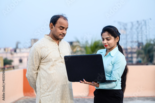 Photography Young indian female in formal dress with laptop showing something to a middle aged man on internet, She is teaching computer and use of technology