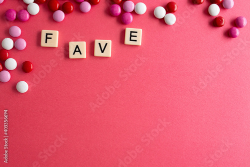 the word fave written as a flat lay in wood scrabble tiles on a plain red background surrounded by red, white, and pink candies photo