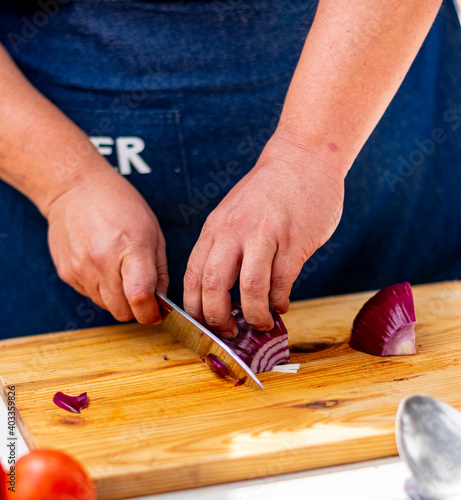 manos con cuchillo cortando cebolla morada en tabla de madera 