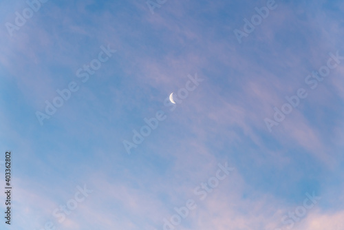 Beautiful blue sky with a partial moon showing on a bright, sunny day with few clouds that have a pink tinge on a crisp winter day. 