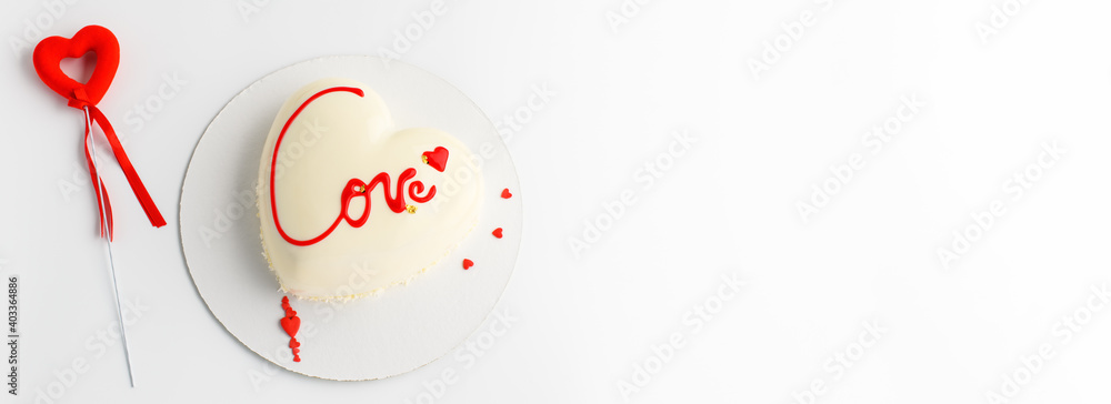 A cake in heart shape.  Mousse light cake in the shape of a heart with the inscription love with red hearts on a gray background. St. Valentine's Day banner for bakery, confectionery. Copy space