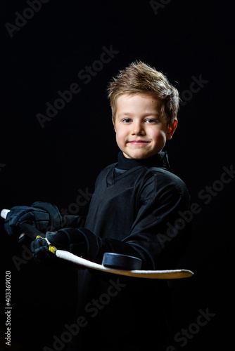a boy hockey player in a black uniform holds a stick with a puck on a black background