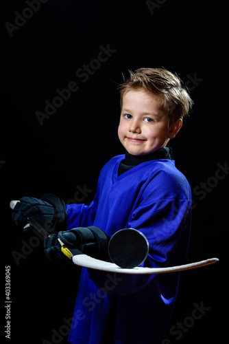 a boy hockey player in a blue uniform holds a stick with a puck on a black background