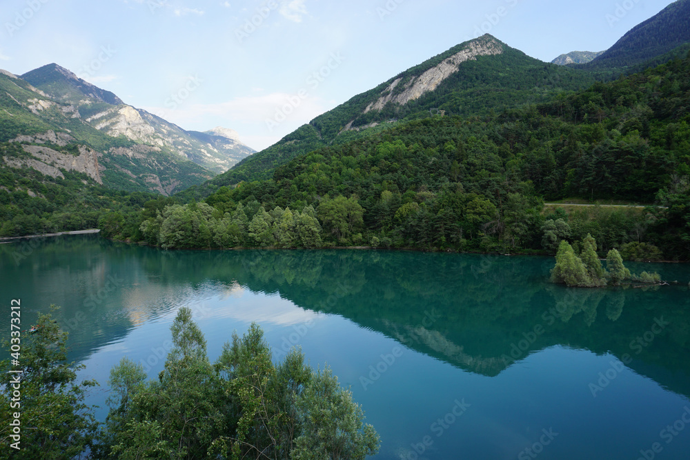 mirror reflection of the mountains and clouds in Serre Ponçon lake, France with a small island