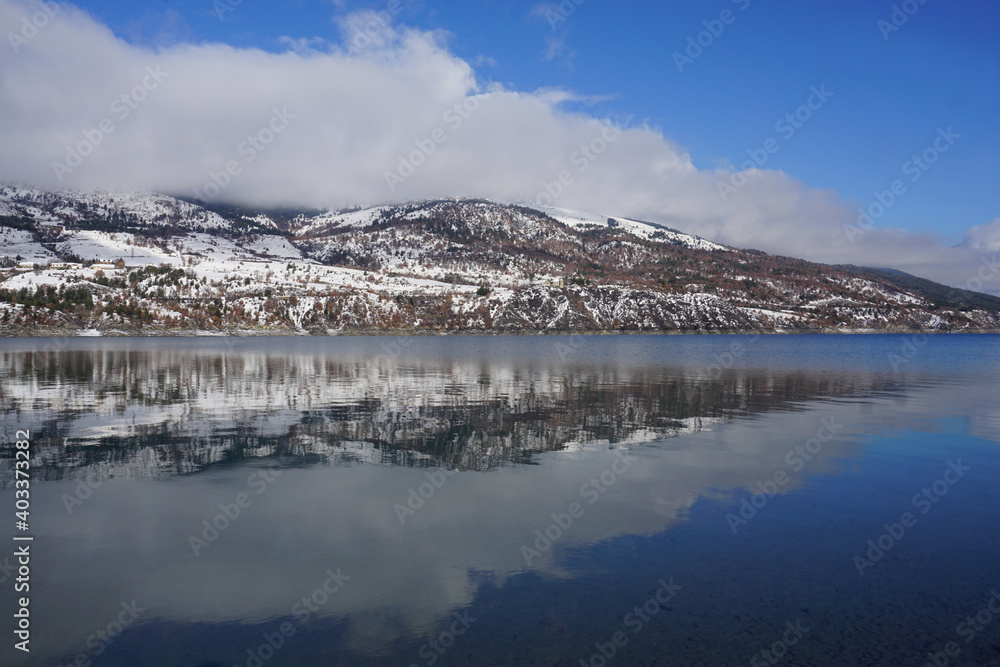 mirror reflection of the mountains and clouds in Serre Ponçon lake, France on a cold winter day