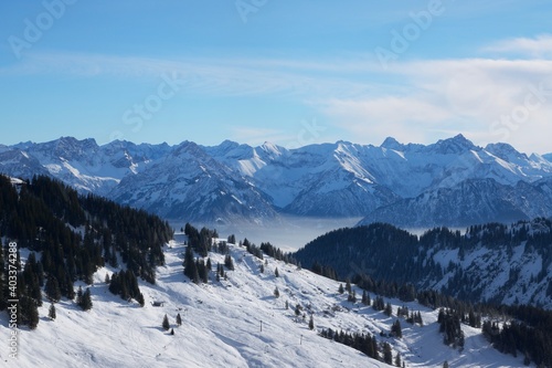 Winterlandschaft der schneebedeckten  bayerischen Alpen über Wolken vor blauem Himmel © Rudolf