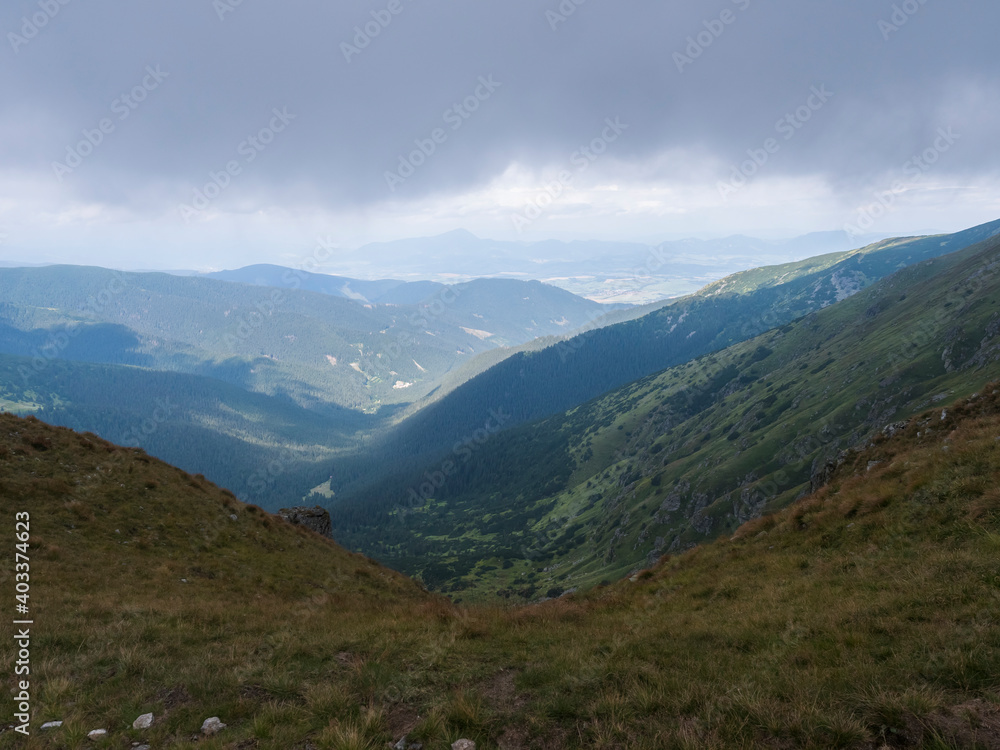 View from grassy hill slopes of hiking trail from Chopok at mountain meadow ridge Low Tatras mountains, Slovakia. Fog and clouds, late summer day