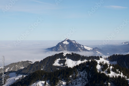 Winterlandschaft der schneebedeckten bayerischen Alpen über Wolken vor blauem Himmel