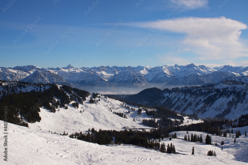 Winterlandschaft der schneebedeckten  bayerischen Alpen über Wolken vor blauem Himmel