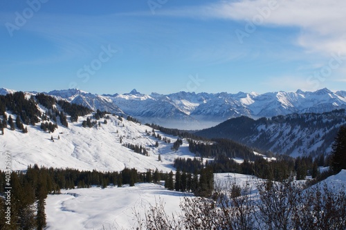 Winterlandschaft der schneebedeckten  bayerischen Alpen   ber Wolken vor blauem Himmel