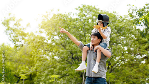 Lifestyle Happy Asian family Father and son sat on his shoulder and run in park. Paper plane as toy in hand of kid And there are many big tree in garden Is natural in morning of summer. Concept travel © Rapeepat