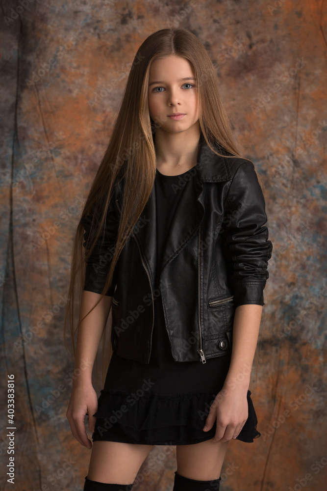 beautiful child girl with long beautiful hair in a black leather jacket on a spotted fabric background