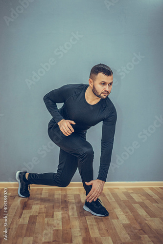 Man stretching his hamstrings. Photo of sporty man doing exercising on grey background. Sports