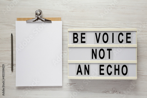 Fototapeta Naklejka Na Ścianę i Meble -  'Be voice not an echo' on a lightbox, clipboard with blank sheet of paper on a white wooden background, top view. Flat lay, overhead, from above.