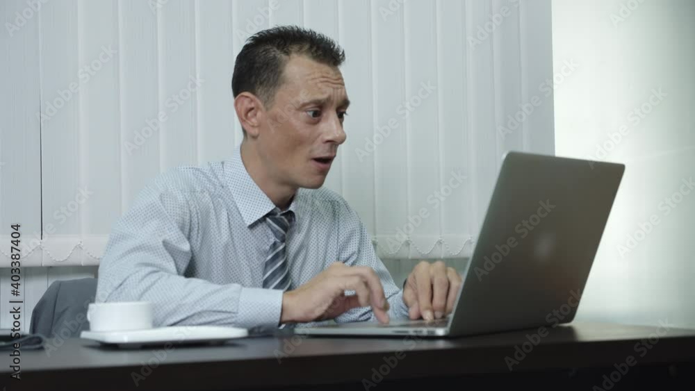 A business man who is a company employee using a laptop to work in an office intensely shocked by his job failure, disappointment and loss in his business anxiously. A business man who is a company employee using a laptop to work in an office intensely shocked by his job failure, disappointment and loss in his business anxiously.