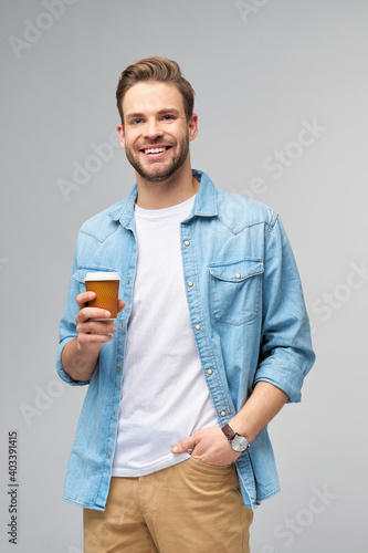 Portrait of young handsome caucasian man in jeans shirt over light background holding cup of coffee to go