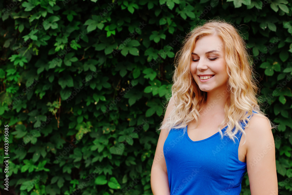 Beautiful young girl smiles in a blue dress, against a background of hedges of wild grapes. Copy space. Beautiful young girl smiles in a blue dress, against a background of hedges of wild grapes. Copy space.