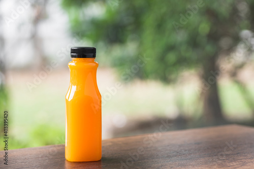 Fresh orange juice in no label clear plastic bottle with black cap on wooden table, natural trees blur in the background. With copy space.