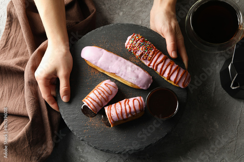 Female hands hold tray with tasty eclairs on gray background