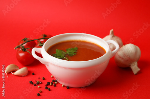Bowl with tomato soup and ingredients on red background
