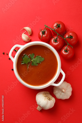 Fotografie Bowl with tomato soup and ingredients on red background