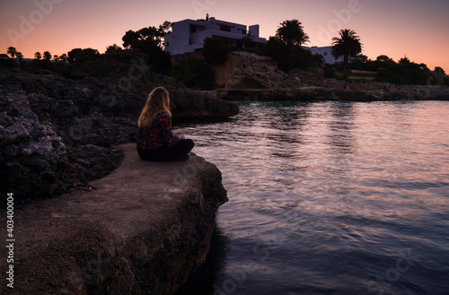 Frau sitzt auf einem Felsen am Wasser an einem Sonnenuntergang