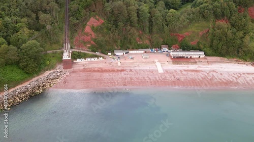 Aerial dolly flight showing popular Oddicombe Beach with blue ocean water, red sand and breccia cliffs, photo