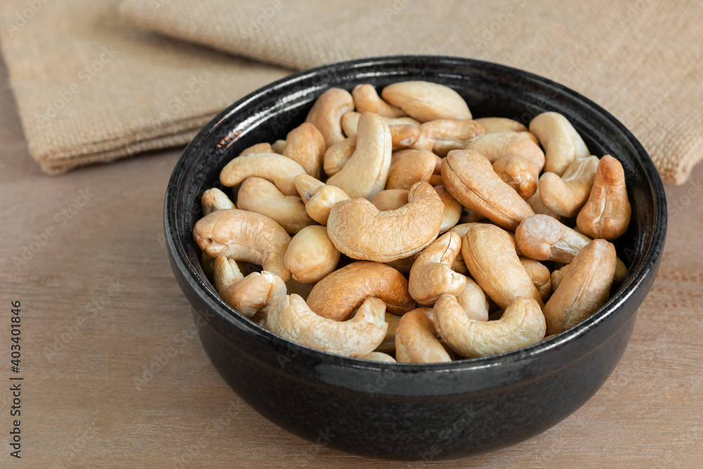 close up of homemade style roasted cashew nuts in a ceramic bowl on wooden table. close up of homemade style roasted cashew nuts in a ceramic bowl on wooden table.