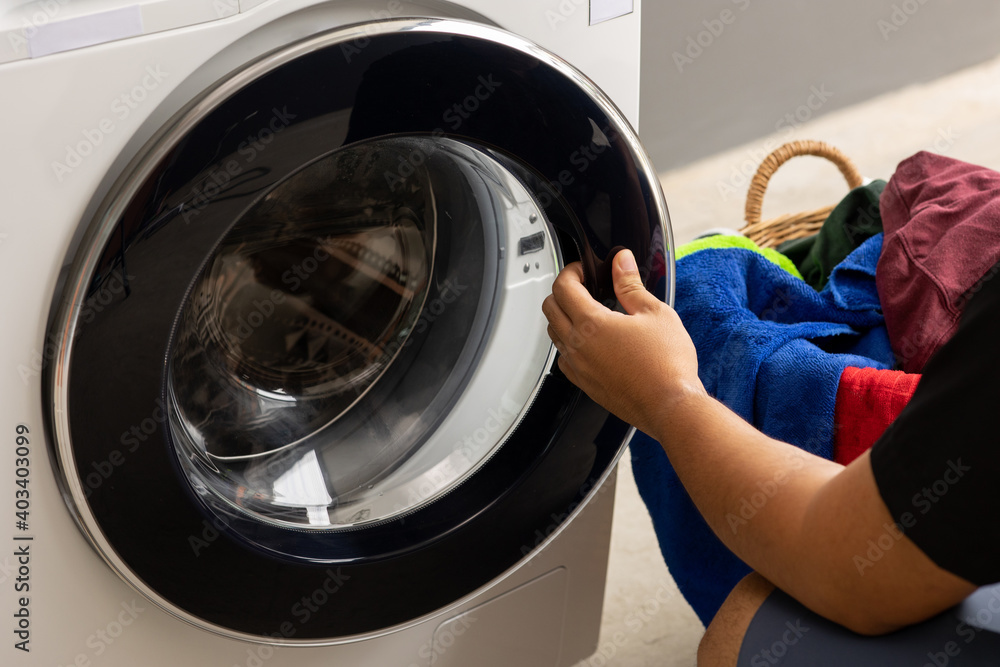 Man's hand opening the front of the washing machine And is about to put the dirty laundry into the wash Man's hand opening the front of the washing machine And is about to put the dirty laundry into the wash