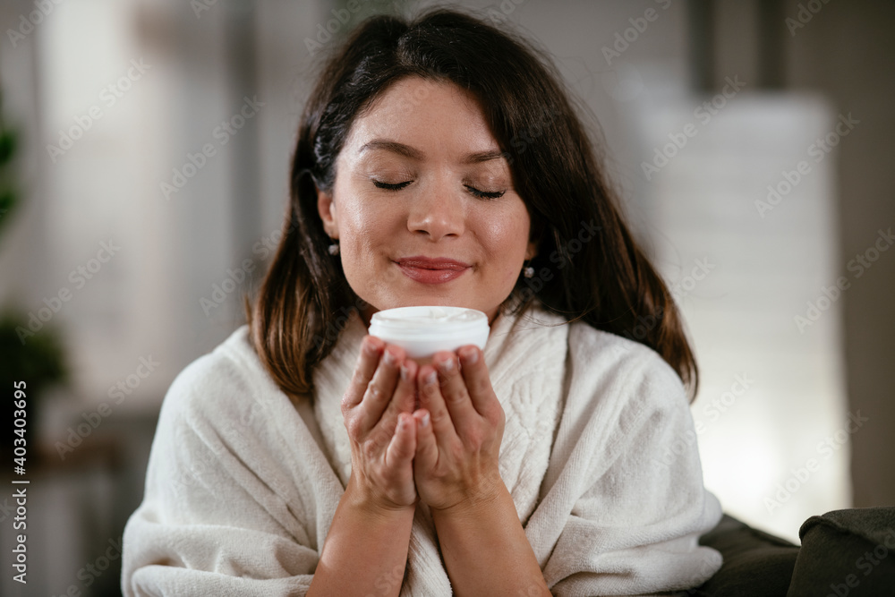 Beautiful woman in bathrobe applying body cream. Smiling woman enjoying after bathing at home. Beautiful woman in bathrobe applying body cream. Smiling woman enjoying after bathing at home.
