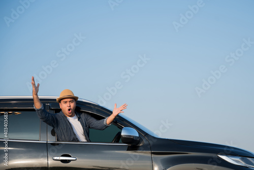 A young Asian man drives a car on a clear day. With beautiful blue sky. He driving to travel by car. © Chanakon