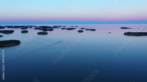 Aerial view of a boat in middle of a lot of small islands, vibrant dusk sky in the Scandinavian archipelago - reverse, drone shot photo