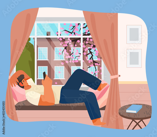 Young man lying on windowsill at home serfing internet with phone. Male character resting in room near big window with spring cityscape view. Spending time at home, relaxing after work, reading
