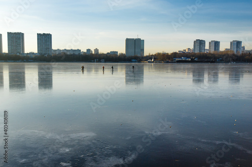People ice skating outdoors on a frozen Moscow river. Reflections of city residential buildings on the ice in front of northern river terminal. Moscow  Russia  December 2020
