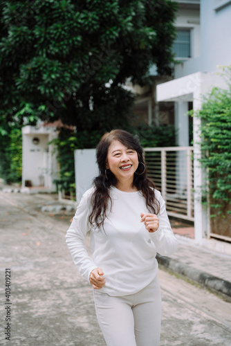 Happy healthy old asian woman in white shirt jogging at street in the morning.