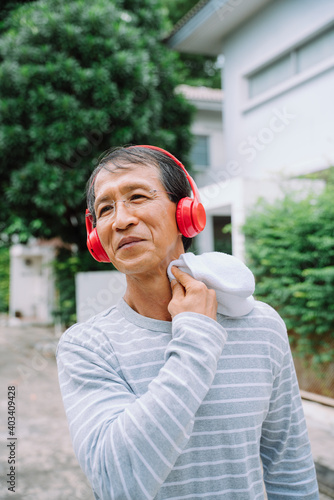 Healthy asian senior man running in a park and listen to music using headphones.