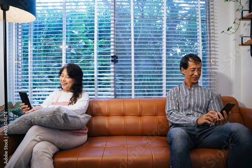 Asian senior couple sitting seperately and using smartphone for talking with each other. photo