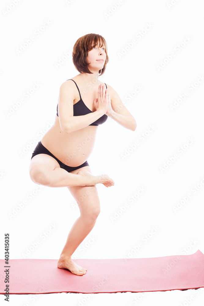 Fototapeta premium Pregnant caucasian woman in black sportswear doing yoga exercises on pink mat isolated on white background.