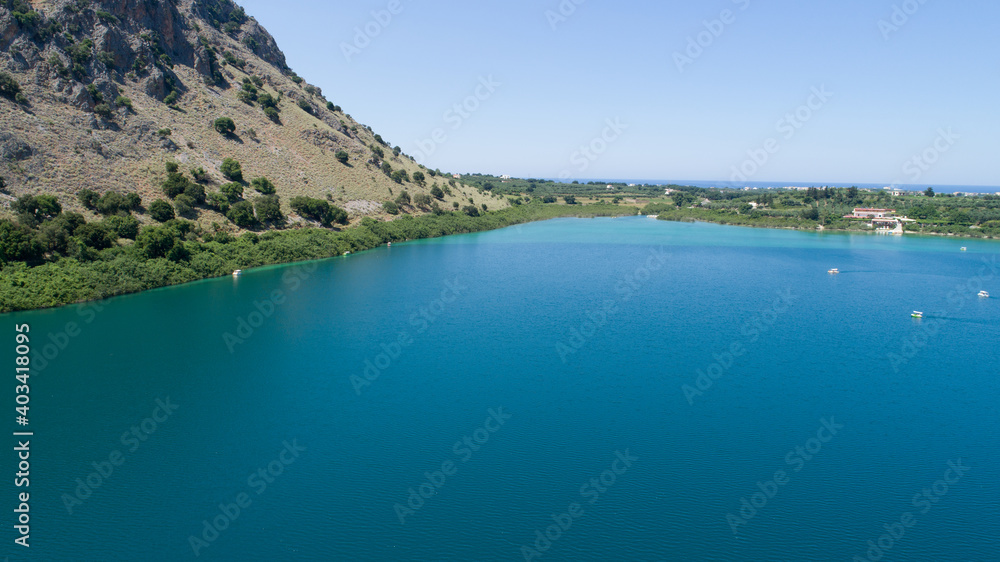 Beautiful scenery of the island from a bird's-eye view. Kataramarans sail along a blue lake against the background of green mountains and the city.