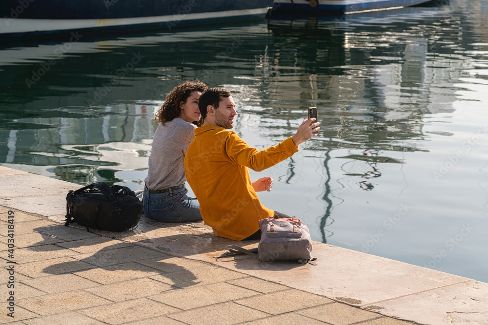Jeune couple assis sur un quai du vieux port de Marseille prend un selfie